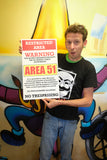 guy holding area 51 warning sign restricted area 13" by 22" vintage style show print poster for size reference in front of a colorful wall painting on a squid man